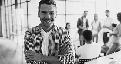 smiling man in an office setting with coworkers in the background